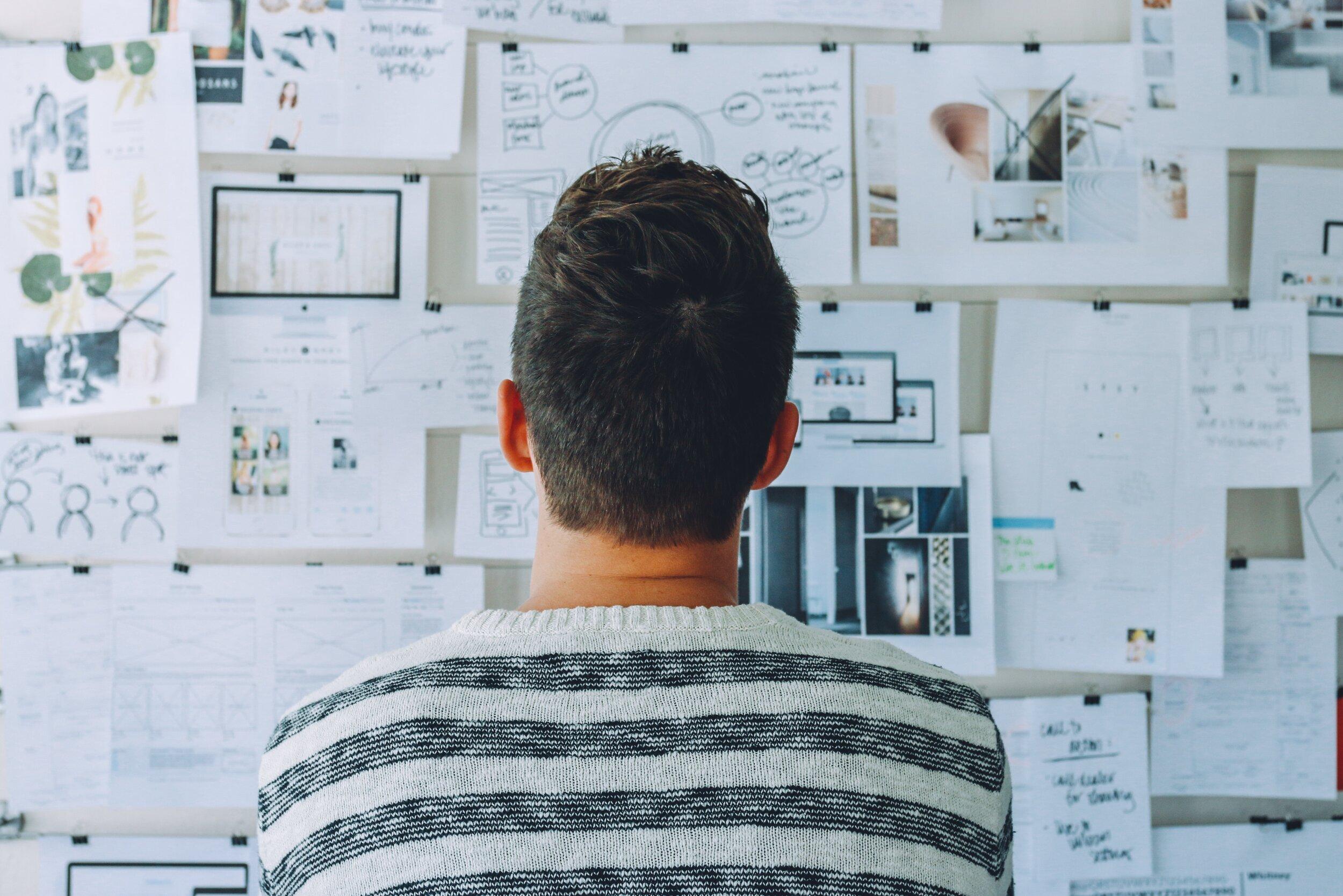 A man reviews a large board filled with lists, charts and other planning materials.