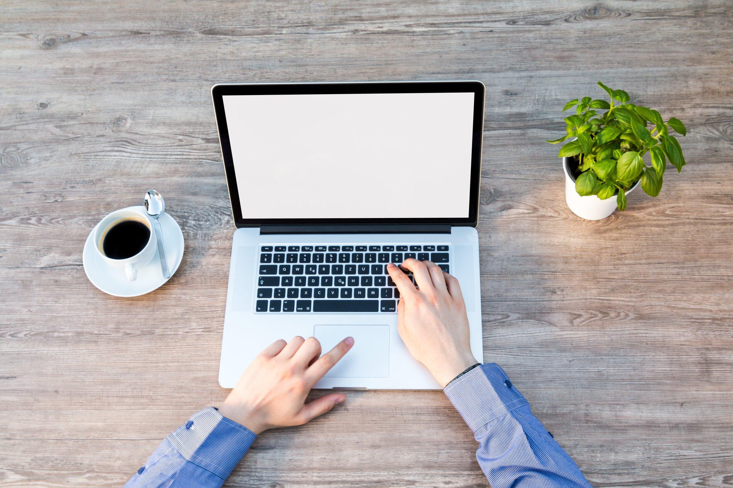 Overhead view of a person’s hands booting up a laptop, with a cup of coffee to the side.